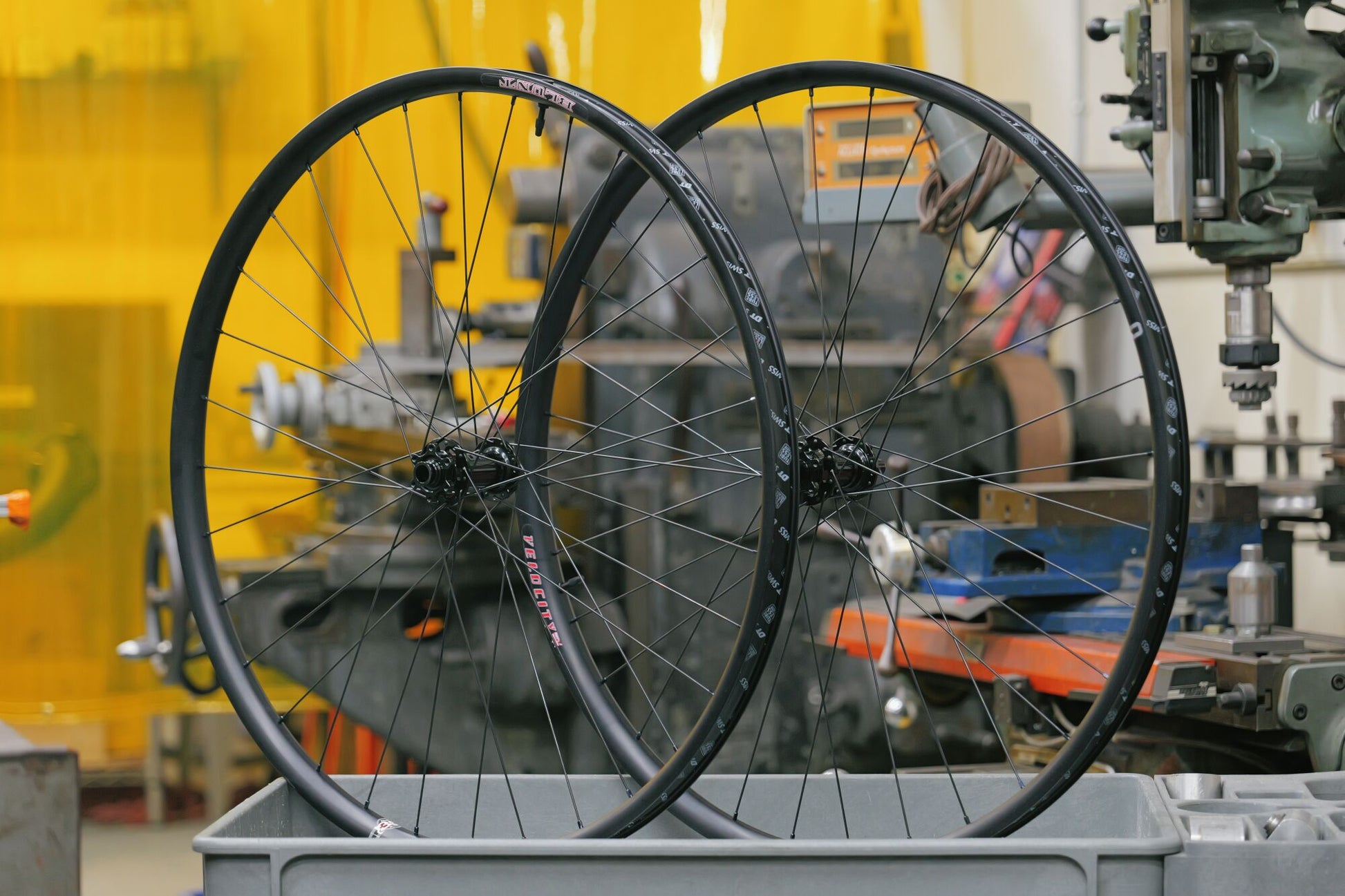 Two bicycle wheels on a workbench with machinery in the background